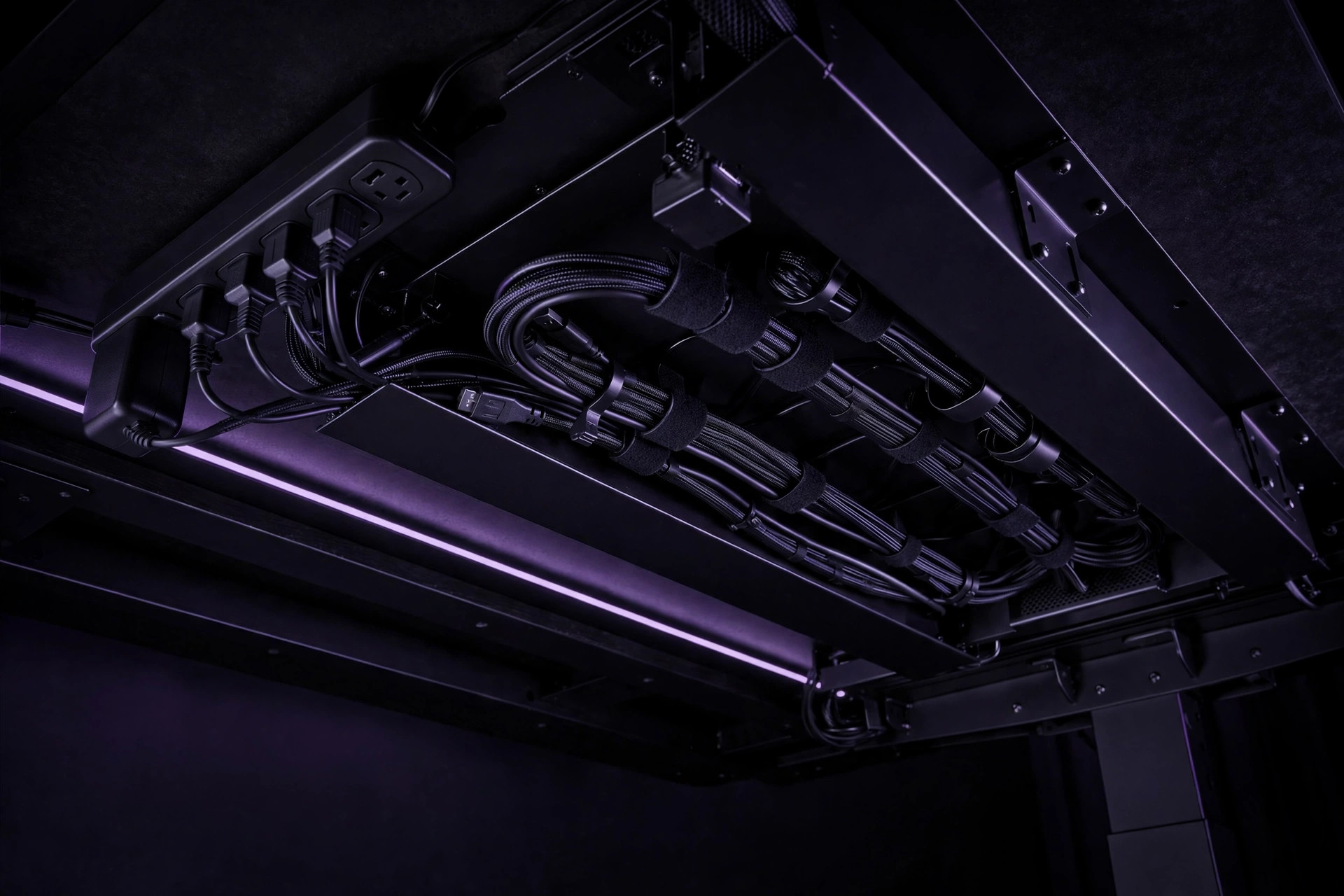 Underside of a desk with cables bundled in straps beside a mounted power strip